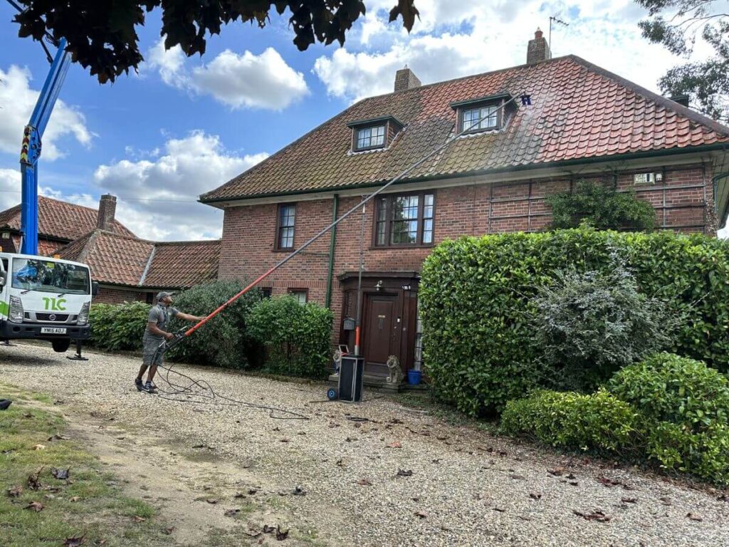 Professional roof cleaning being carried out on a large detached house using long-reach equipment.
