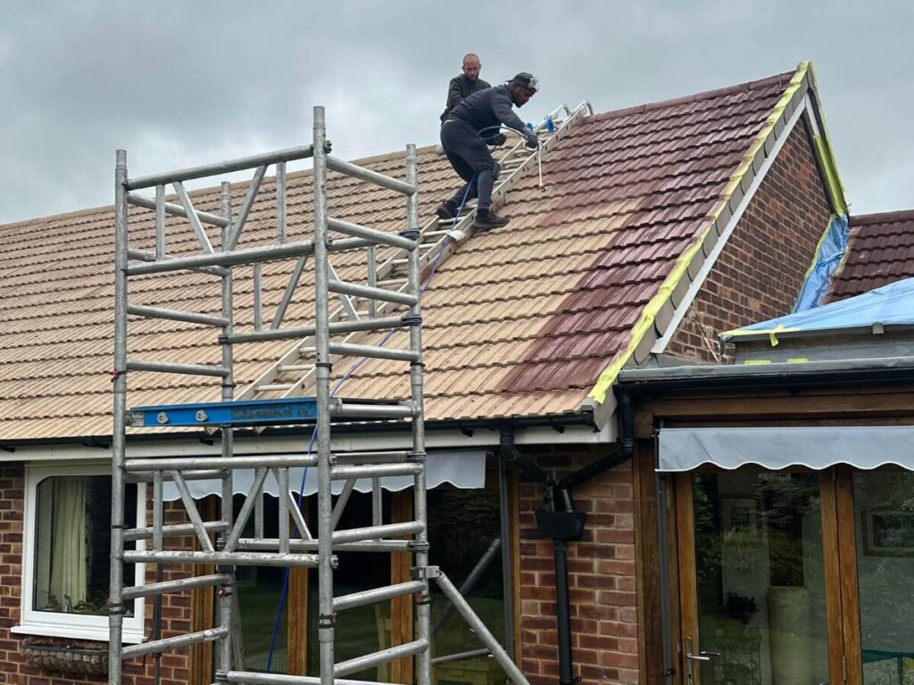 Roof cleaning specialists working from scaffold access as the natural colour of the roof tiles is enhanced.