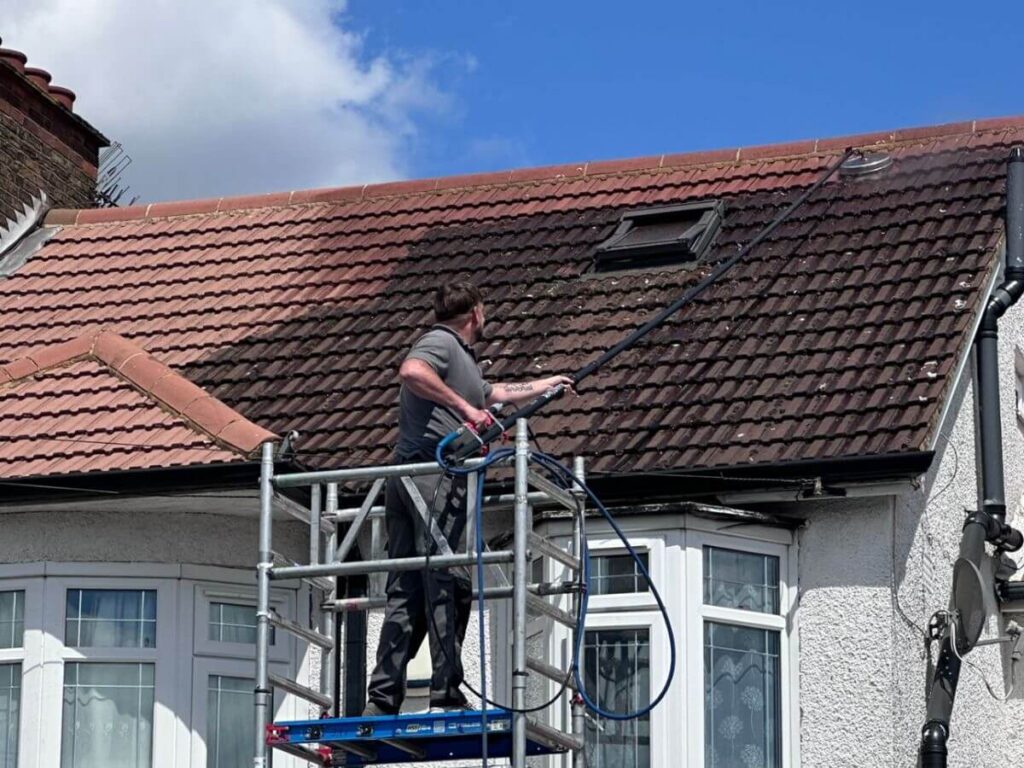 Roof cleaning specialist using scaffold tower to clean a residential tiled roof, showing a clear before and after comparison.